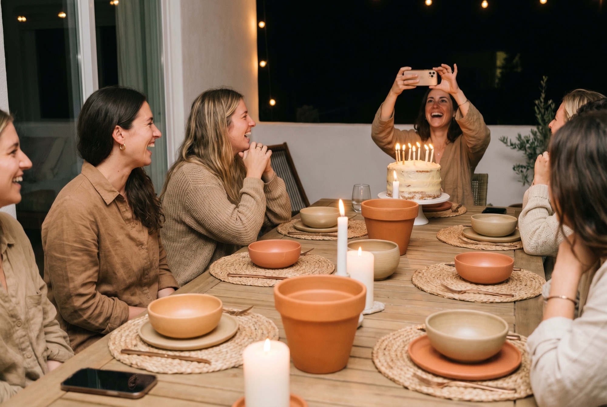 A candlelit birthday dinner as a guest photographs the cake.